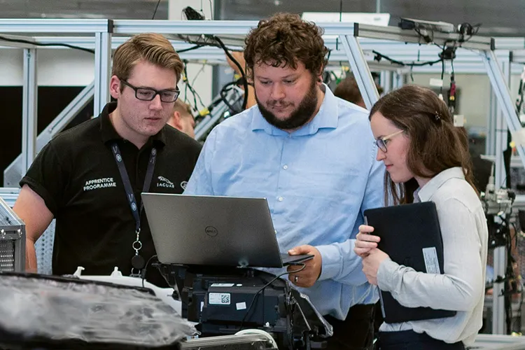 employees around a computer in a factory setting asking questions